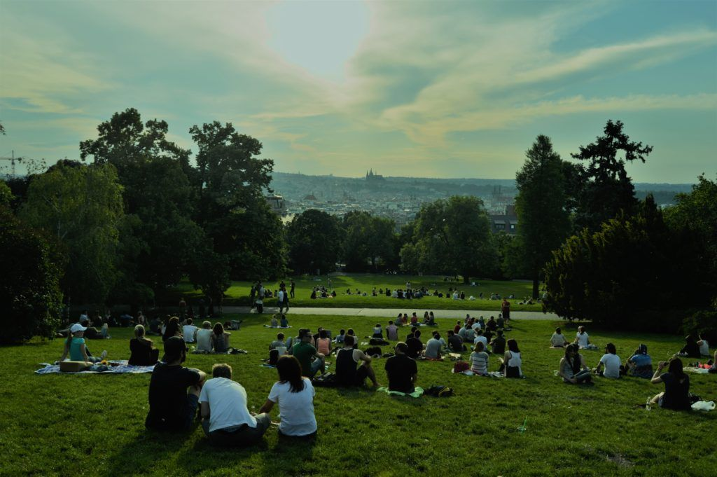 A group of people sitting on a grassy hillside watching the sunset over Prague in Riegrovy Sady Park.